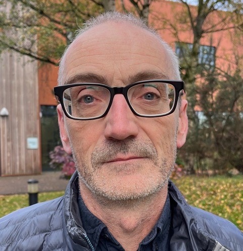 A portrait of Professor Andrew Weller outside in the autumn wearing glasses.