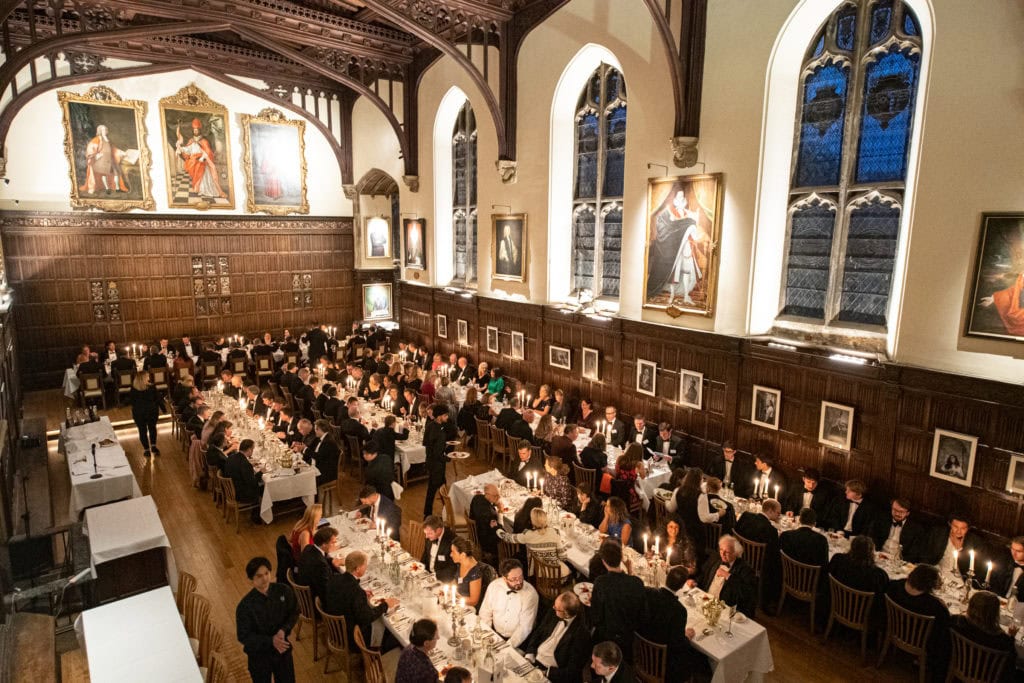 People sit around long tables in Magdalen College hall