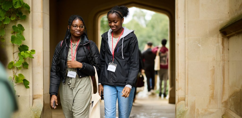 Two students walking in Magdalen cloisters smiling while chatting.