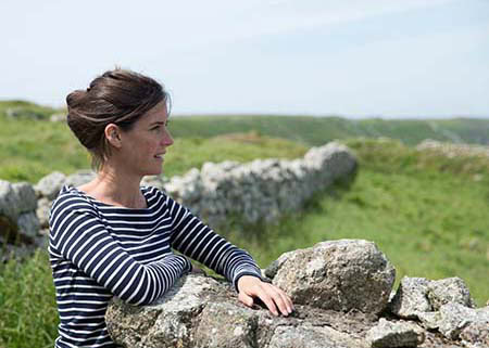Picture of Dr Anna Keay looking to the right of the frame surrounded by dry stone walls and country views