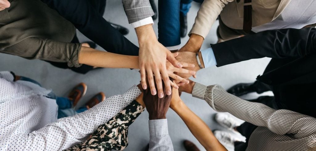 a shot of many hands belonging to people of different races centred in the frame.