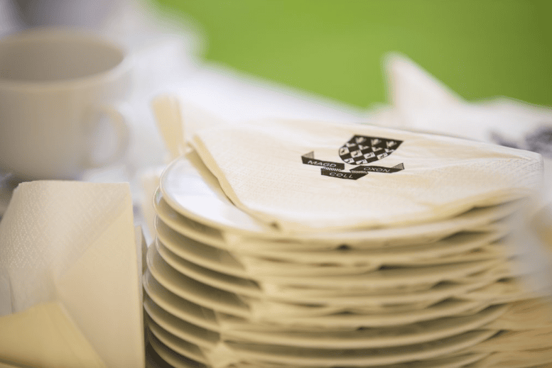 a stack of plates with napkins on them that read MAGD COLL OXON topped by a black an white version of our crest.