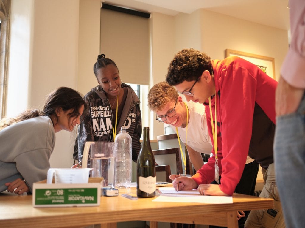 students standing round a table smiling, looking at bottles and writing on paper