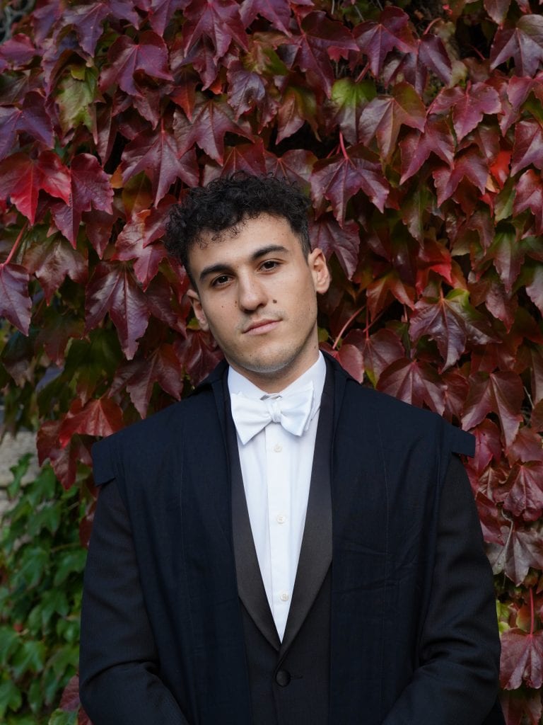a portrait of charles wearing sub fusc in front of foliage