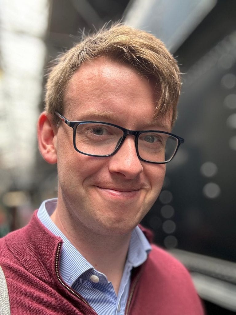 a portrait of Thomas Kelly smiling and wearing glasses