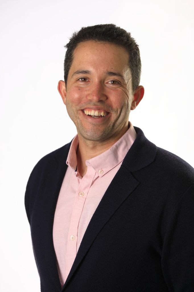 a portrait of Professor Jordan English smiling wearing a black jacket and a pink shirt on a white background
