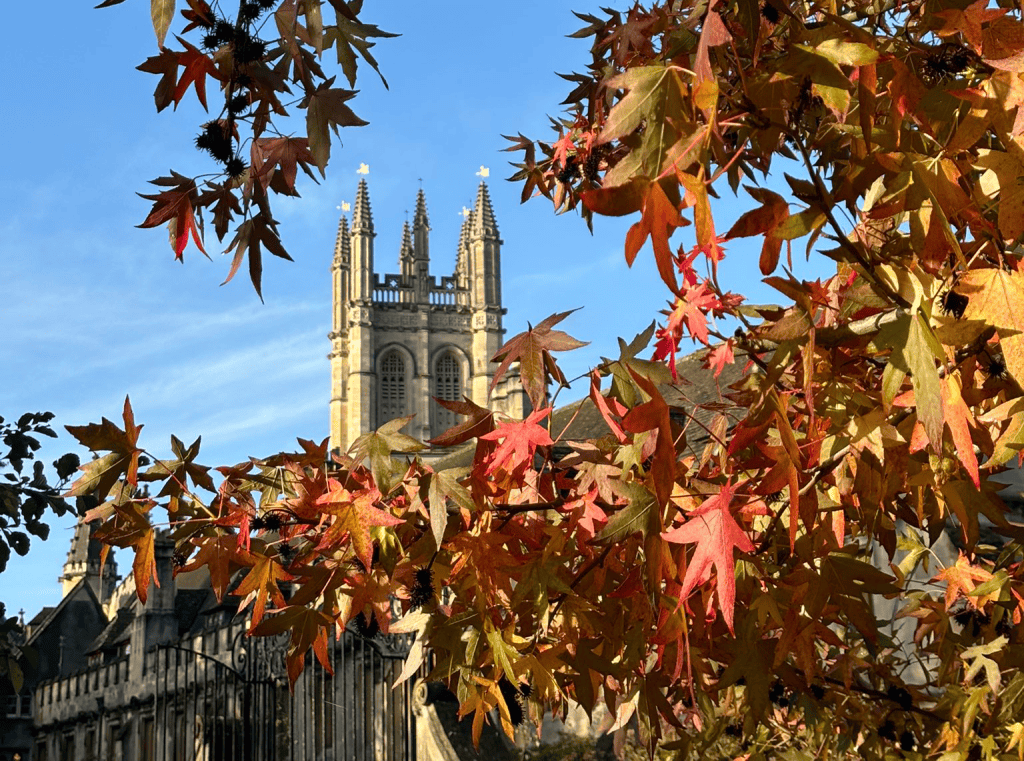 A photograph of the tower with four golden flag weather vanes on each pinnacle, surrounded by blue skies and orange and red autumnal leaves