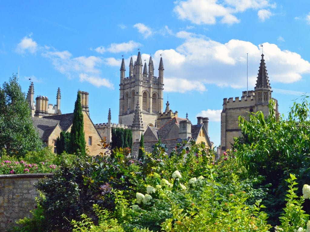 a view of College from the Grove. The borders are in full flower, and the sky is blue with a few clouds