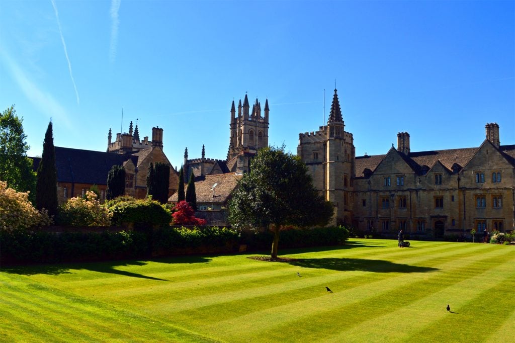 A view of the college from St Swithun's Quad showing the mawn being mown in high summer. Three crows dot the lawn, and the sky is a high and cloudless blue