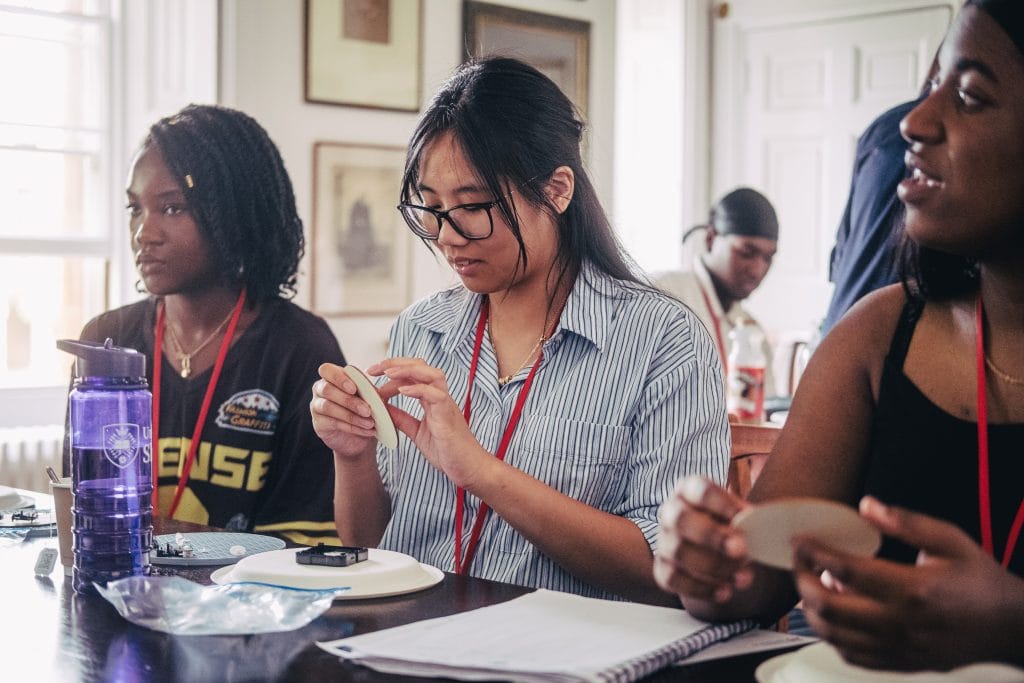 Three girls at a desk, making clocks.