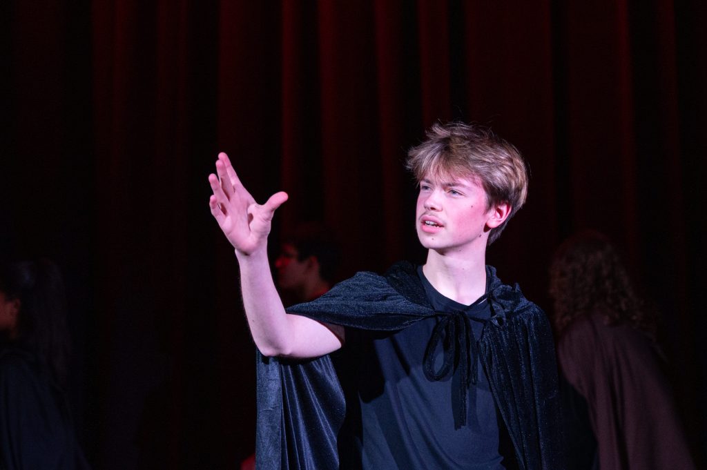 A boy looks just off-camera with hand outstretched, mid-monologue speech.