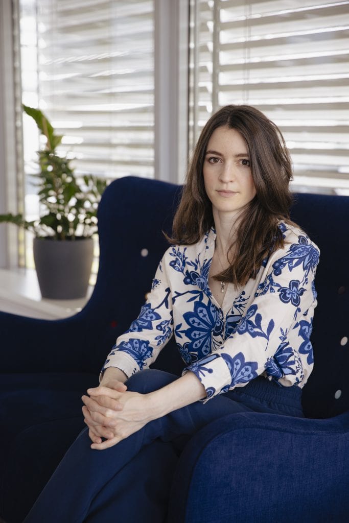Dr Julia Ebner is sat on a sofa, hands folded, looking at the camera