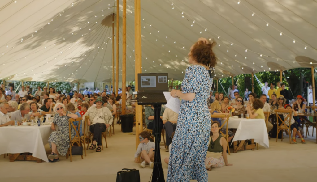 A wide shot of dinah addressing a crowd of alumni and friends in a marquee.