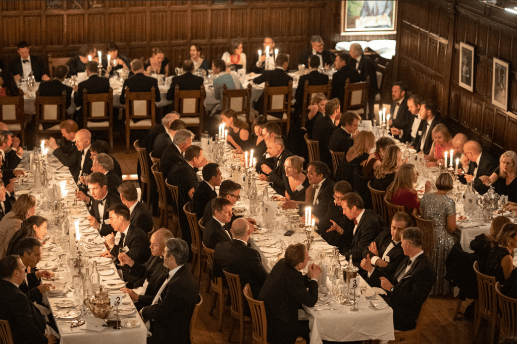 People sit around long tables chatting and laughing in a grand hall