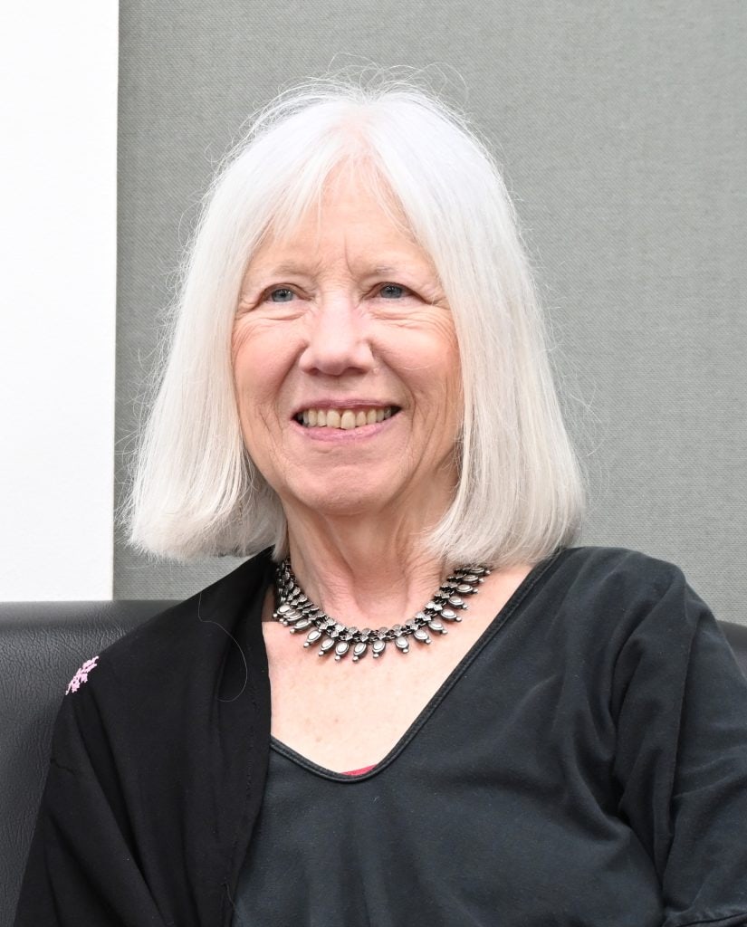A portrait of Marilyn Booth in a black shirt against a grey background.