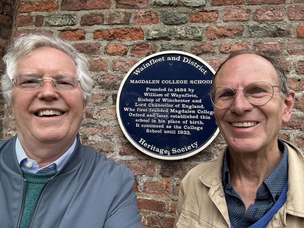 A photo of two men in front of the Wainfleet and District Heritage society plaque. It reads: Magdalen College School, Founded in 1484 by William of Waynflete, Bishop of Winchester and Lord Chancellor of England who first founded Magdalen College, Oxford and later established this school in his place of birth. It continued as the College School until 1933.