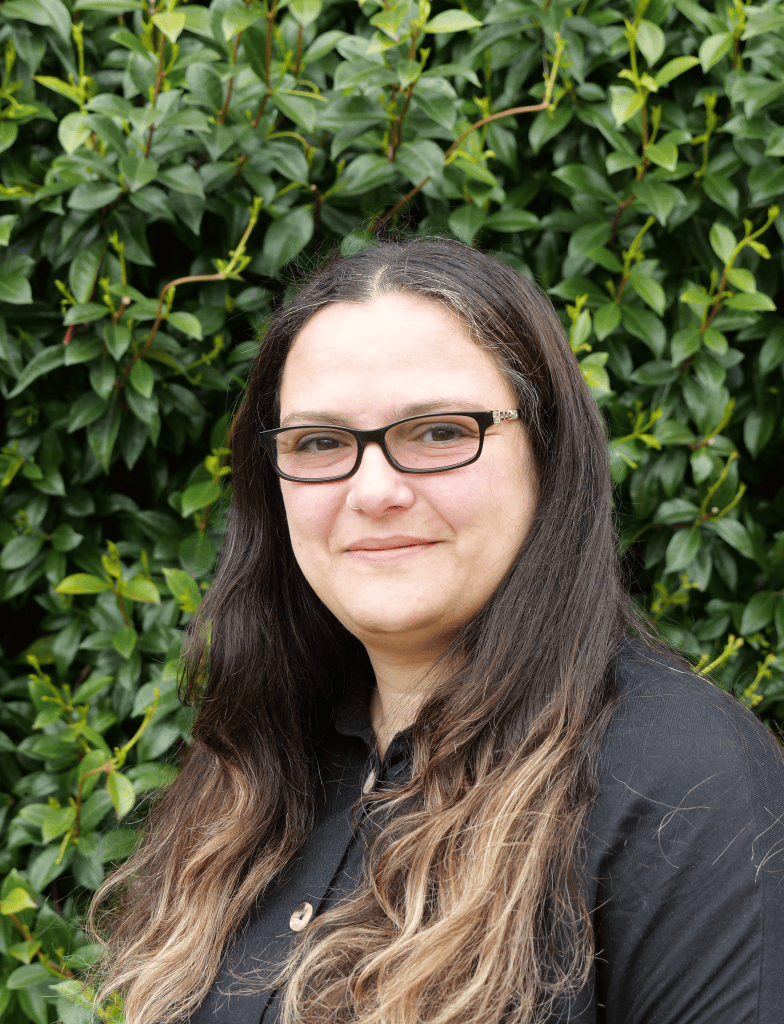 A portrait of Nadia wearing a black shirt against a dark green leafy background