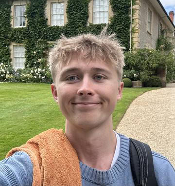 A slefie of angus against a green ivied wall wearing a blue jumper