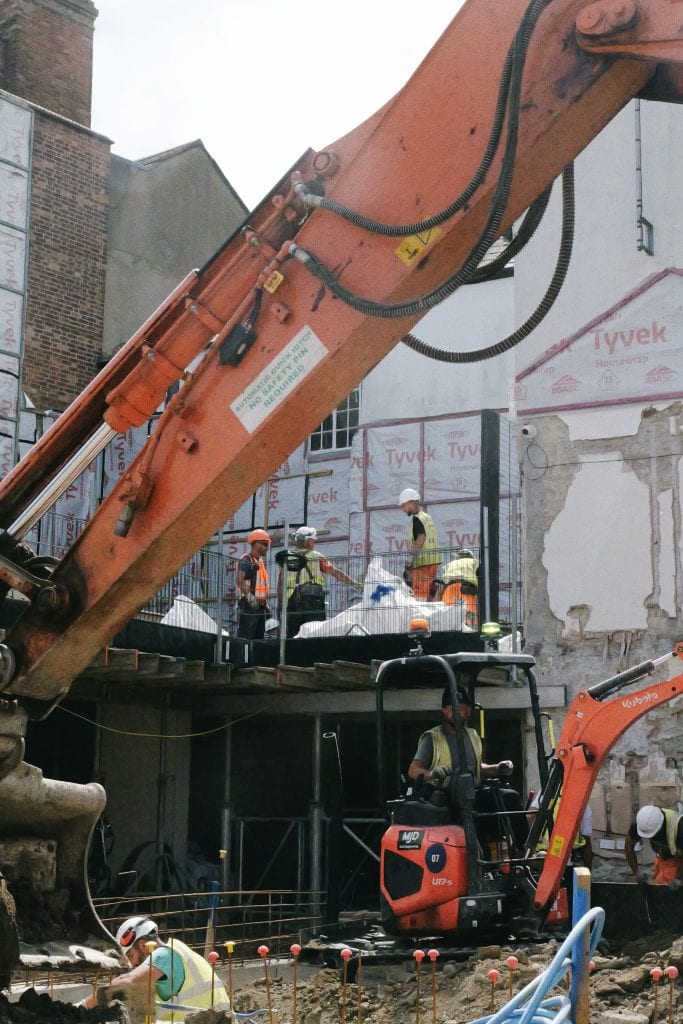 Builders working on the Waynflete site with the arm of a digger in the foreground
