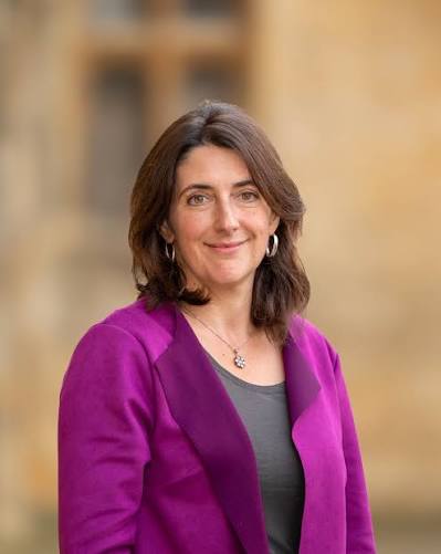 Laura swift is photographed infront of Oxford stone wearing a purple jacket, smiling.